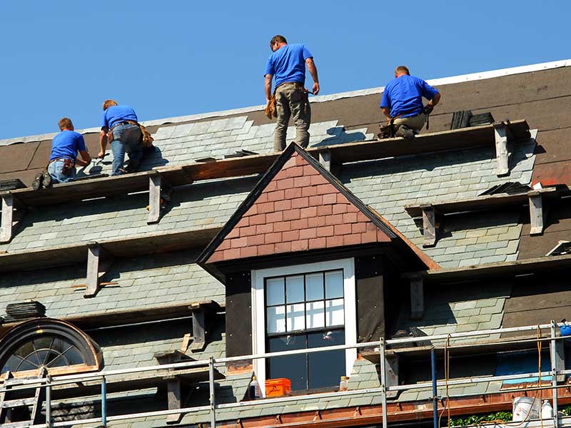 Close-up of workers replacing old shingles on a tall residential home